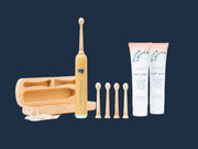 A bamboo electric toothbrush with a matching bamboo charging case, five replacement brush heads, and two tubes of oral care cream on a clean white background.
